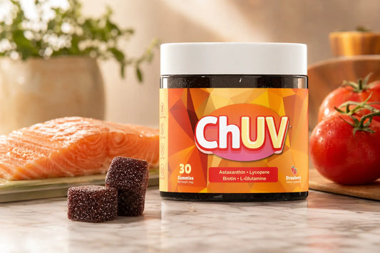 ChUV tanning gummies jar with dark reddish-purple sugar-coated gummy cubes beside wild-caught salmon and ripe red tomatoes on white marble, warm natural studio lighting, the antioxidant power of astaxanthin editorial lifestyle